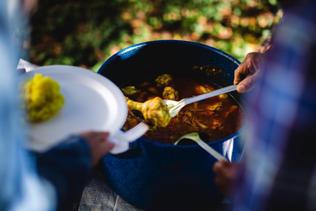 Hands serve stewed chicken from a metal pot