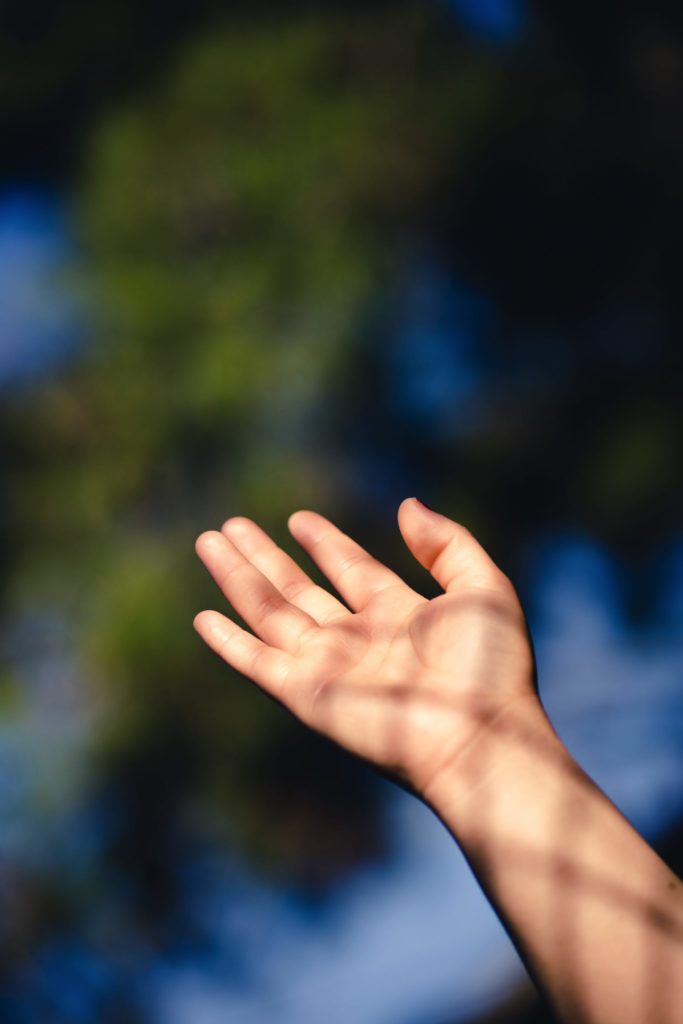 A child's hand reaches up into the sky