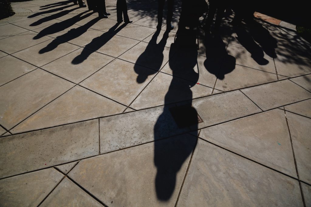 Image: several shadows stand together on a stone pavement.